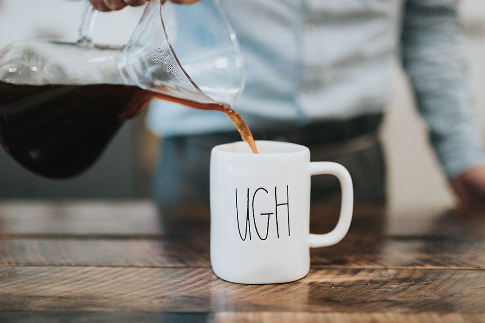 Man pouring coffee into a white mug with the word UGH written on it.